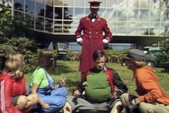 Kuva: Kaasiset ja Kaakot paistavat makkaraa hotellin nurmella ja vahtimestari saapuu paikalle. YLE kuvanauha. 